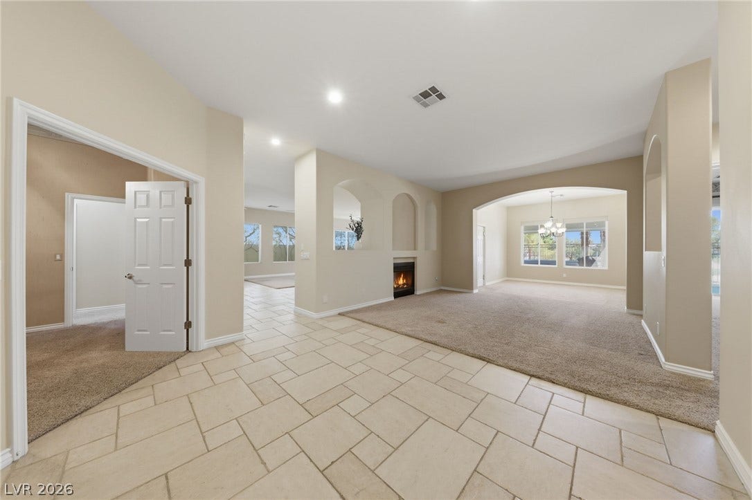 Arched transitions connect tiled pathways to carpeted living zones accented by a modern fireplace.