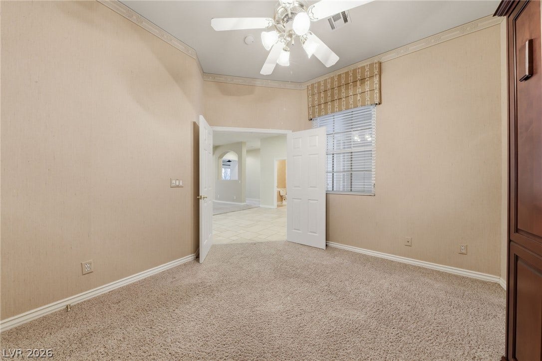 Double doors open to a carpeted bedroom with high ceilings and detailed crown molding.