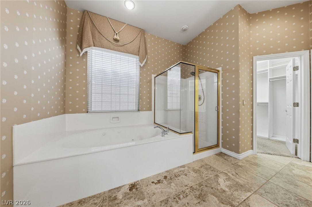 High ceilings and stone tile flooring elevate this bathroom featuring a separate soaking tub.