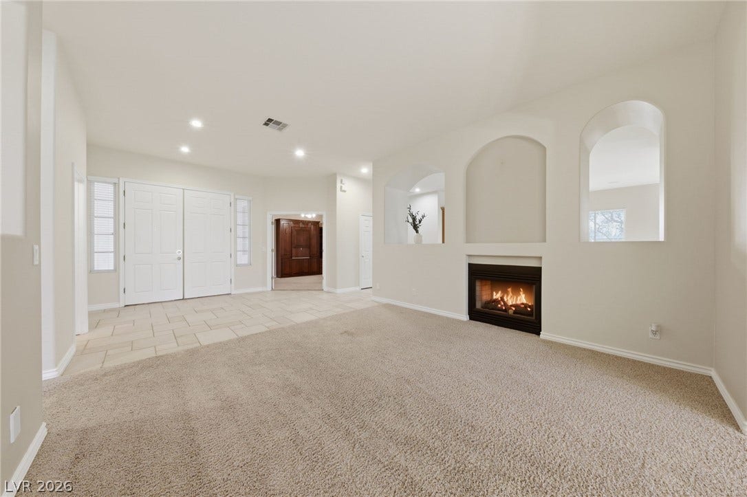 An inviting fireplace warms this open living space featuring soft carpet and arched wall cutouts.