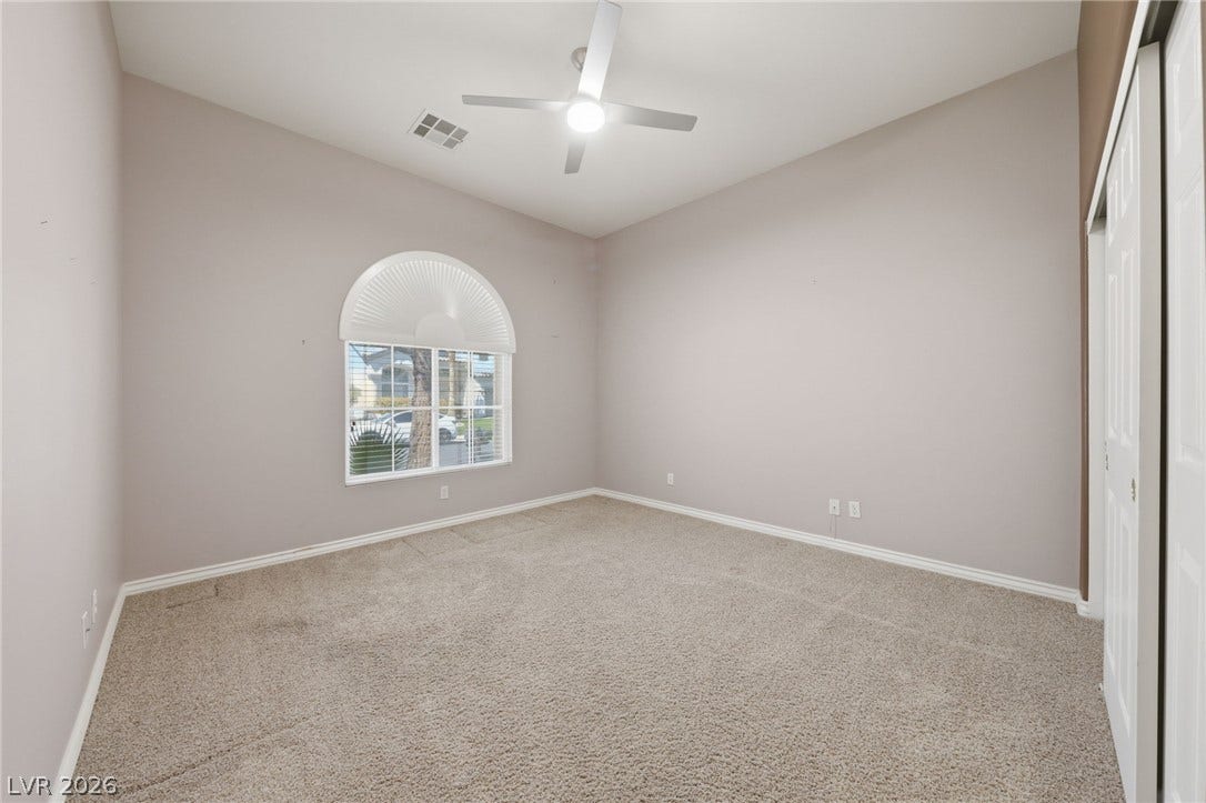 An arched window lets natural light stream onto the neutral carpeting of this versatile bedroom.