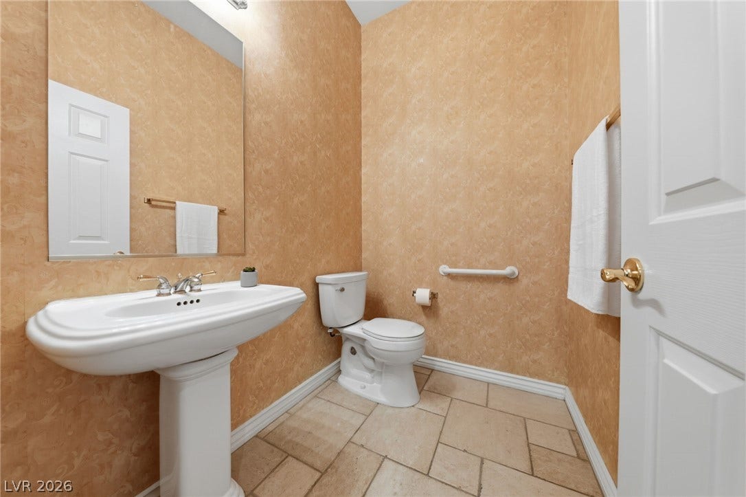 A classic pedestal sink paired with neutral tile flooring coordinates within this warm powder room.