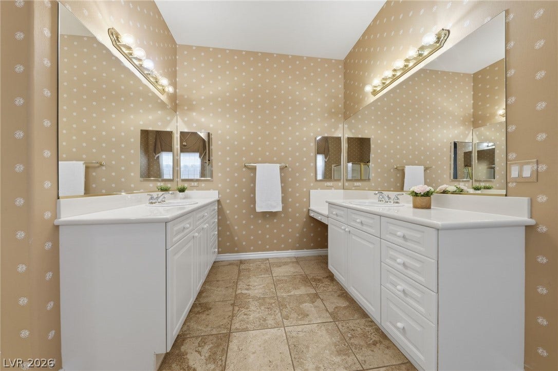 Dual vanities flank a central walkway featuring patterned wall coverings and tiled flooring.