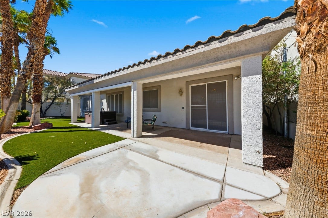 An expansive covered patio overlooks the manicured lawn under clear blue skies.