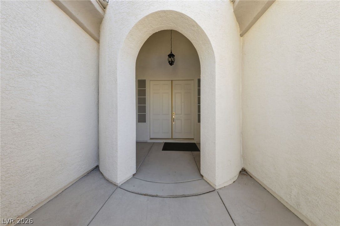 An arched entryway features double doors and stucco walls leading into the home.
