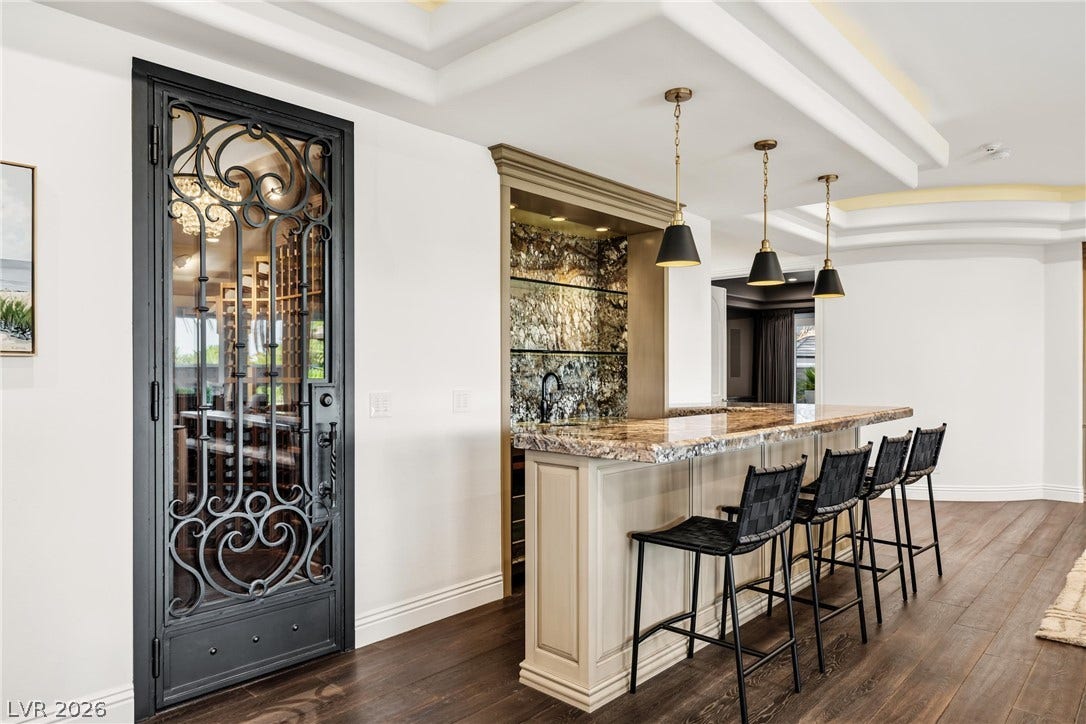 9817 Mountain Grove Court, Las Vegas, NV 89134 Rich wood flooring and tiered ceilings frame a custom home bar with stone countertops.