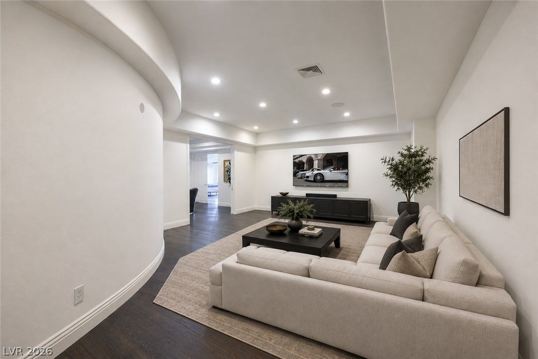 9817 Mountain Grove Court, Las Vegas, NV 89134 A curved gallery wall guides entry into a light-filled living area featuring dark wood floors.