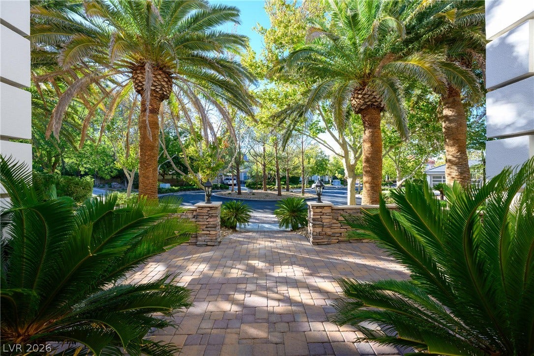 9817 Mountain Grove Court, Las Vegas, NV 89134 Lush palm trees flank a beautifully paved stone courtyard entry under sunny blue skies.