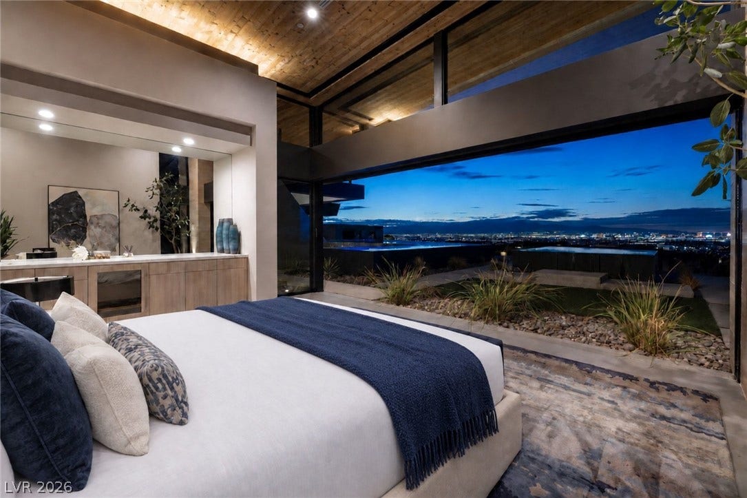 705 Dragon Peak Drive, Henderson, NV 89012 Dramatic floor-to-ceiling windows look out to twinkling city lights from this modern bedroom.