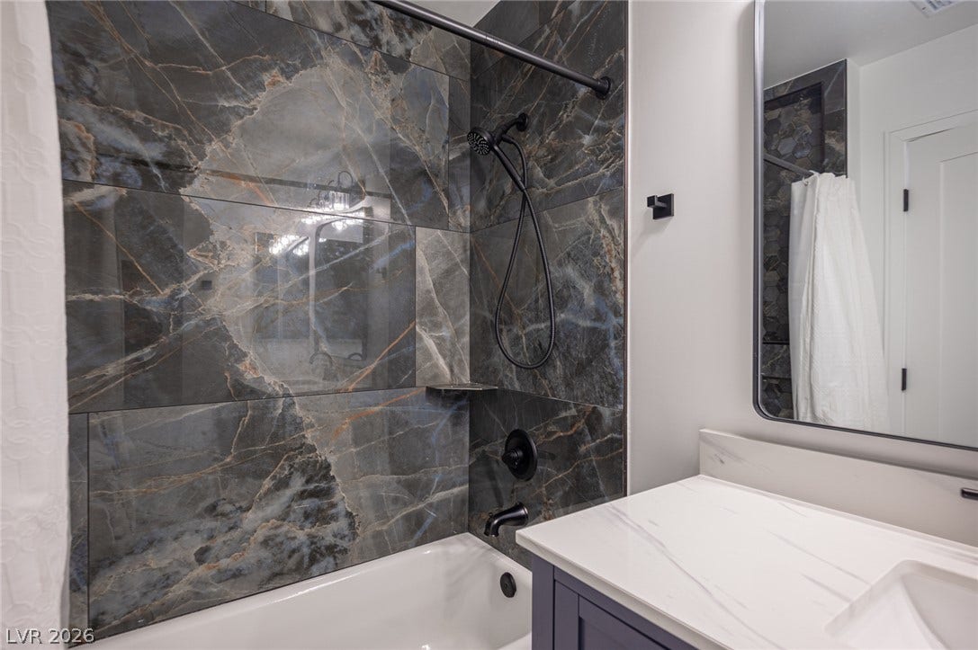 3139 Regal Oak Drive, Henderson, NV 89014 Dramatic dark marble-patterned tile surrounds the bathtub paired with a sleek stone vanity top.