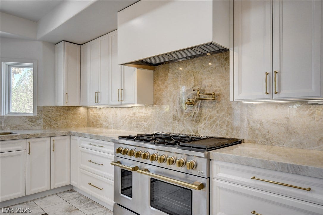Gleaming stone countertops and matching full-height backsplashes frame a professional-grade gas range.