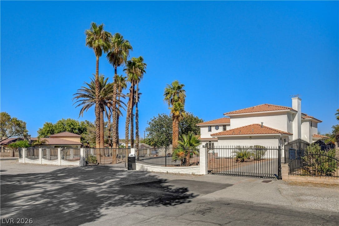 An elegant gated driveway leads to this Mediterranean-style residence framed by towering palm trees.