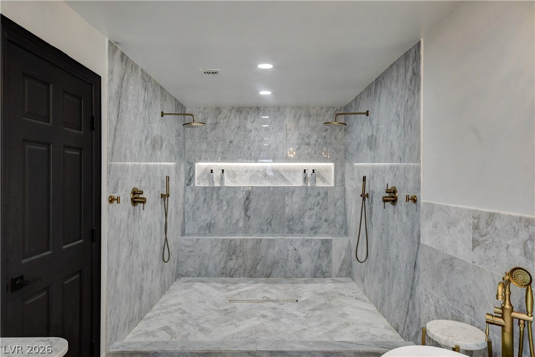 Indulge in a walk-in shower wrapped in premium stone tile and elegant fixtures.