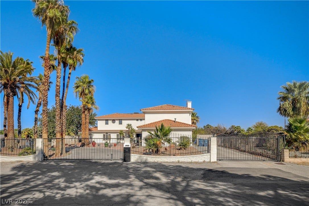 A secure gated entrance opens to the expansive paved driveway of this multi-level stucco estate.
