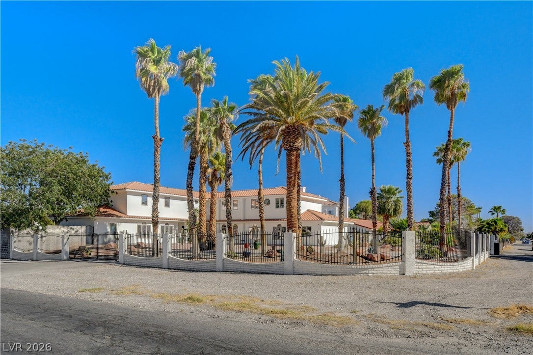Soaring palm trees frame this grand multi-level estate wrapped in elegant wrought iron fencing.