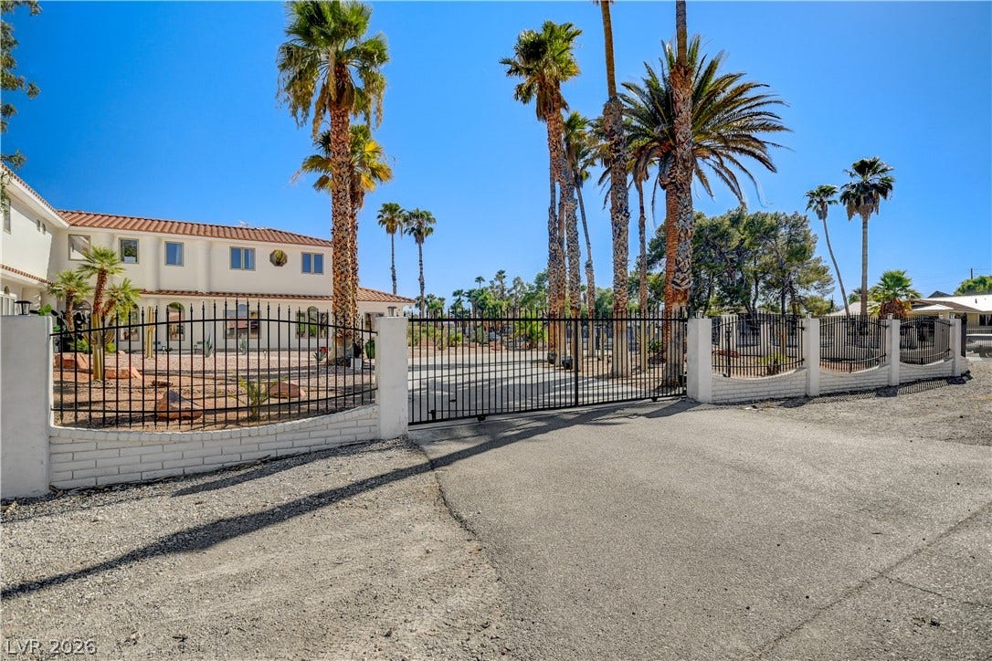Secure gated entry opens to a spacious driveway surrounded by mature palm trees.