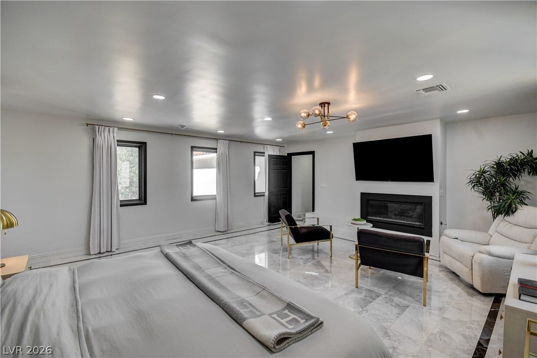 Polished stone flooring, recessed lighting, and a modern fireplace anchor this expansive primary suite.