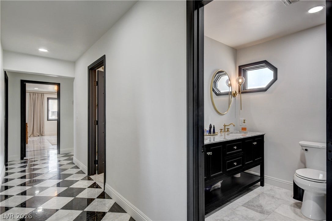 Striking dark-trimmed doorways connect a patterned hallway to a modern bathroom with marble floors.