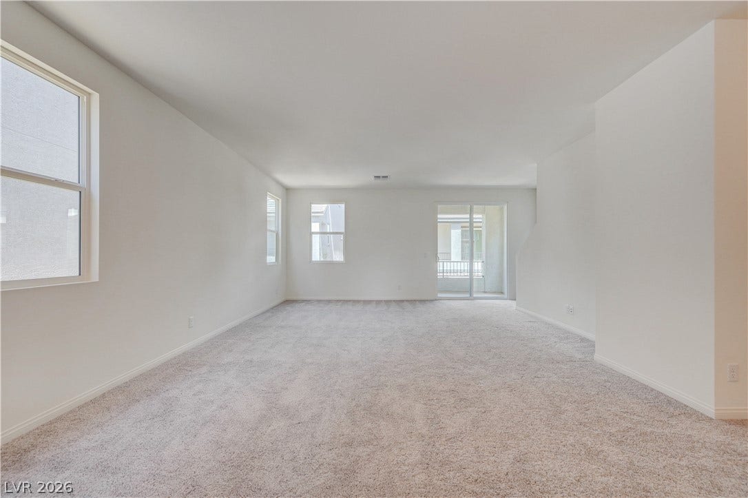 Plush carpeting and multiple windows define this open interior layout leading to outdoor access.
