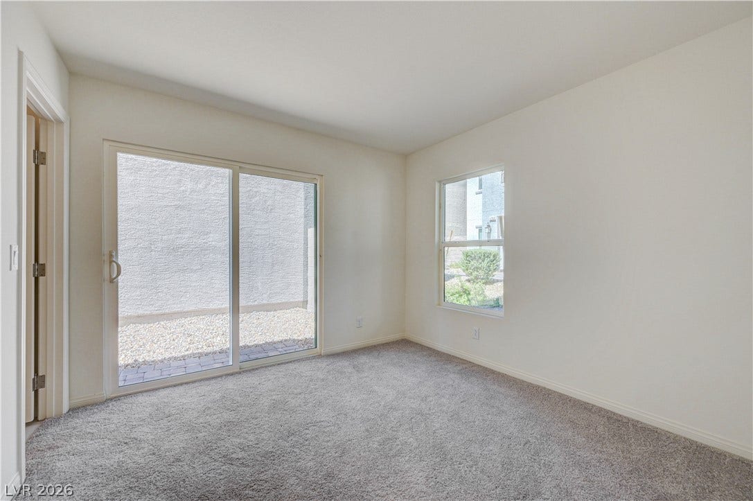 Sliding glass doors open directly to a private gravel courtyard from this carpeted bedroom.
