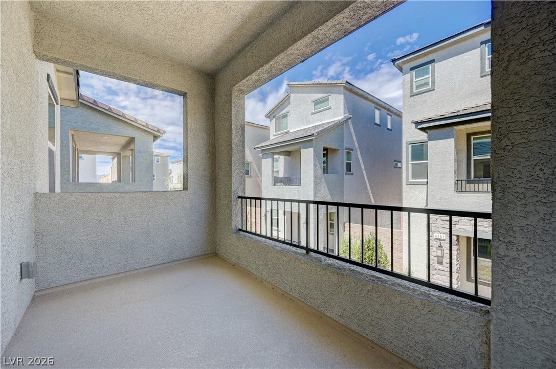 Covered stucco balcony overlooks a quiet neighborhood setting under blue skies.