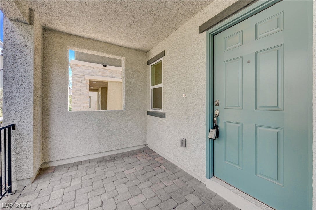 A covered entryway features textured stucco walls and classic paver stone flooring.