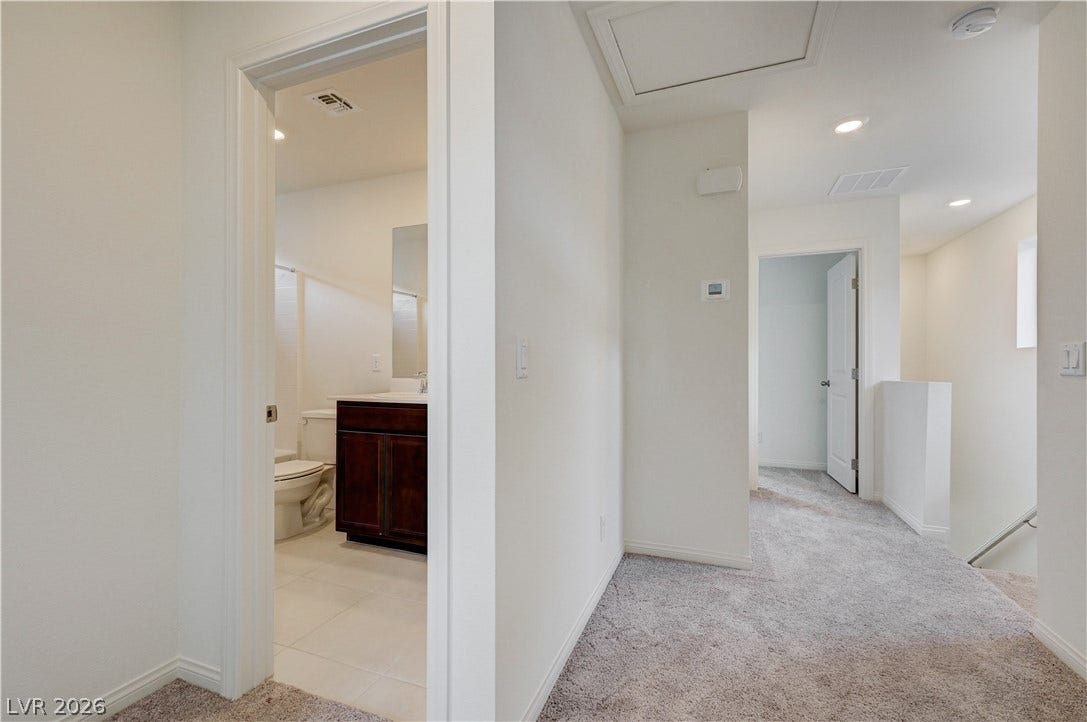 A spacious carpeted hallway connects several rooms and showcases smooth drywall finishes.