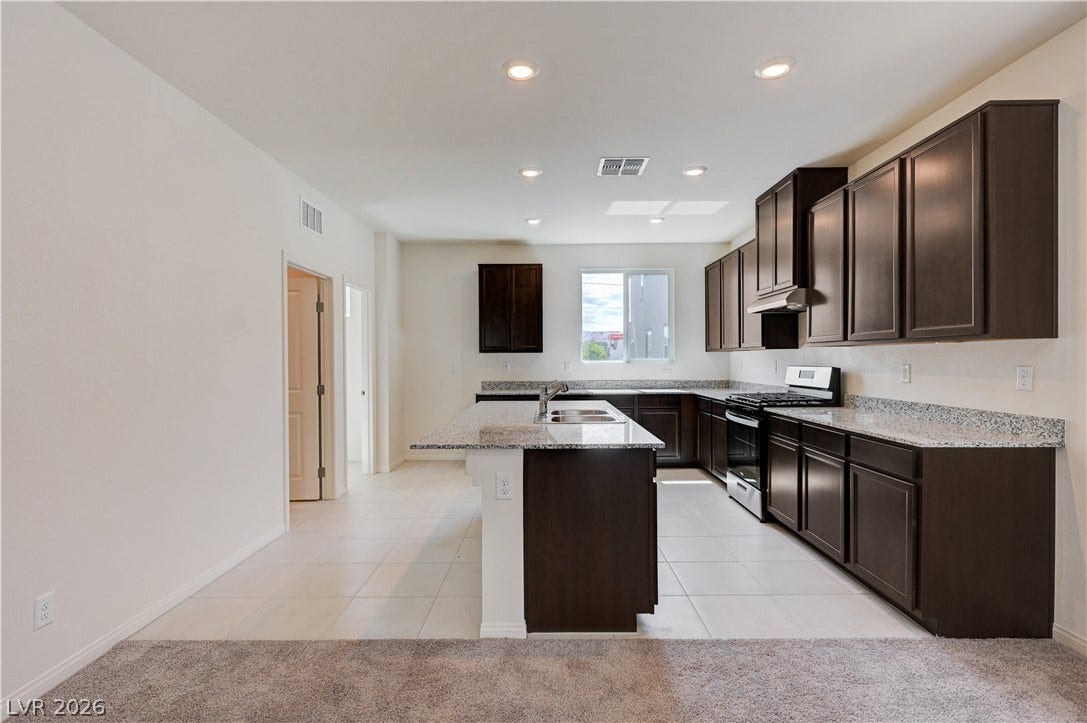 Granite countertops and dark cabinetry define this open kitchen with tiled flooring.