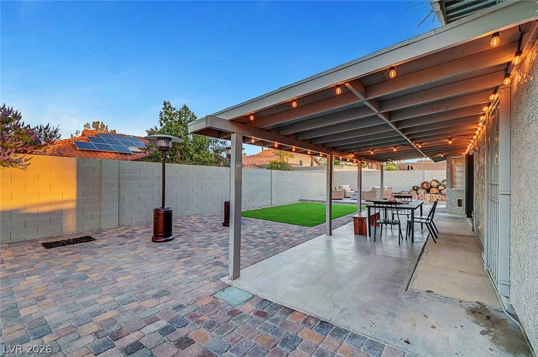 An inviting covered patio opens to a paved backyard with a manicured green lawn.