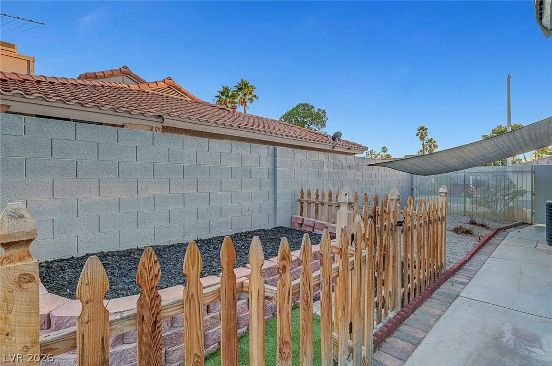 An enclosed backyard area features brick retaining walls, wooden picket fencing, and concrete pathways.