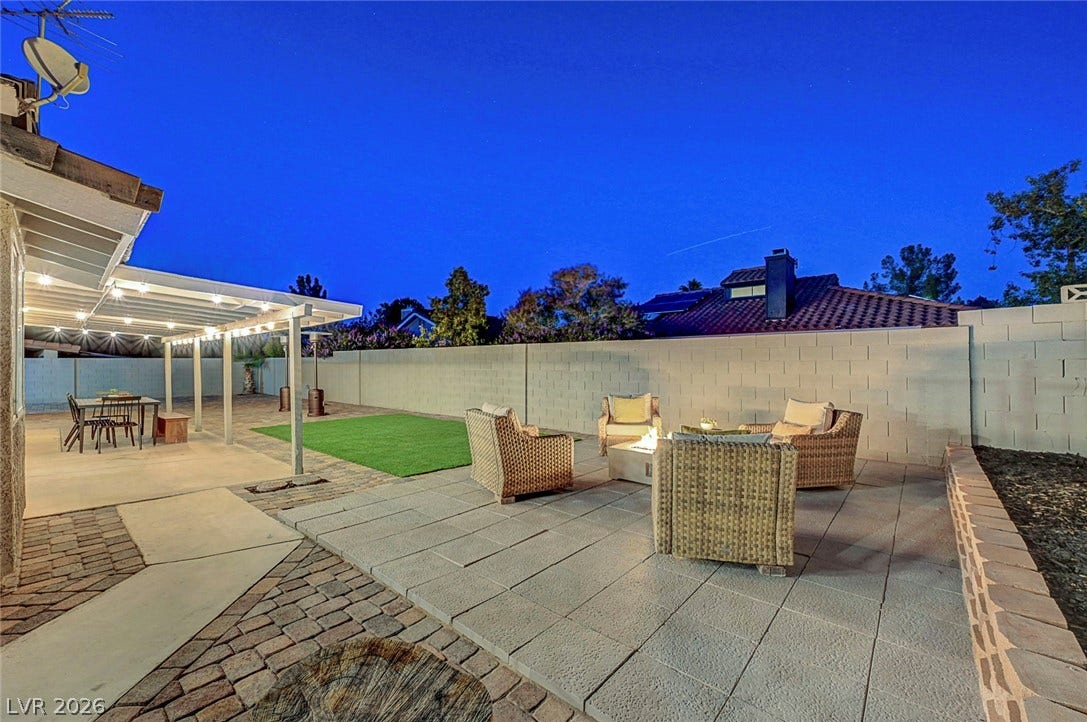 An inviting stone patio and manicured lawn are enclosed by a privacy wall under open skies.