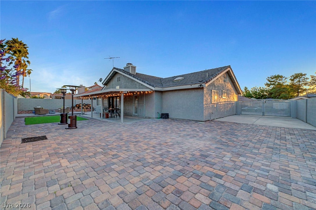 An expansive paver patio sits under clear blue skies behind a stucco home.