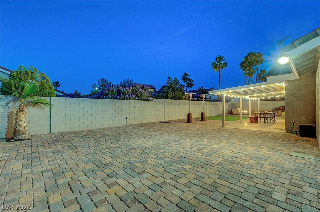 An expansive paved patio extends from the covered porch, flanked by secure block fencing.
