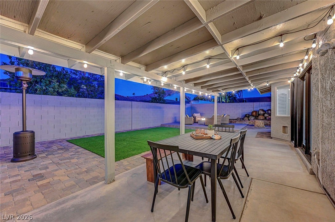 A sheltered concrete patio overlooks a brick-paved terrace and neat grassy yard.