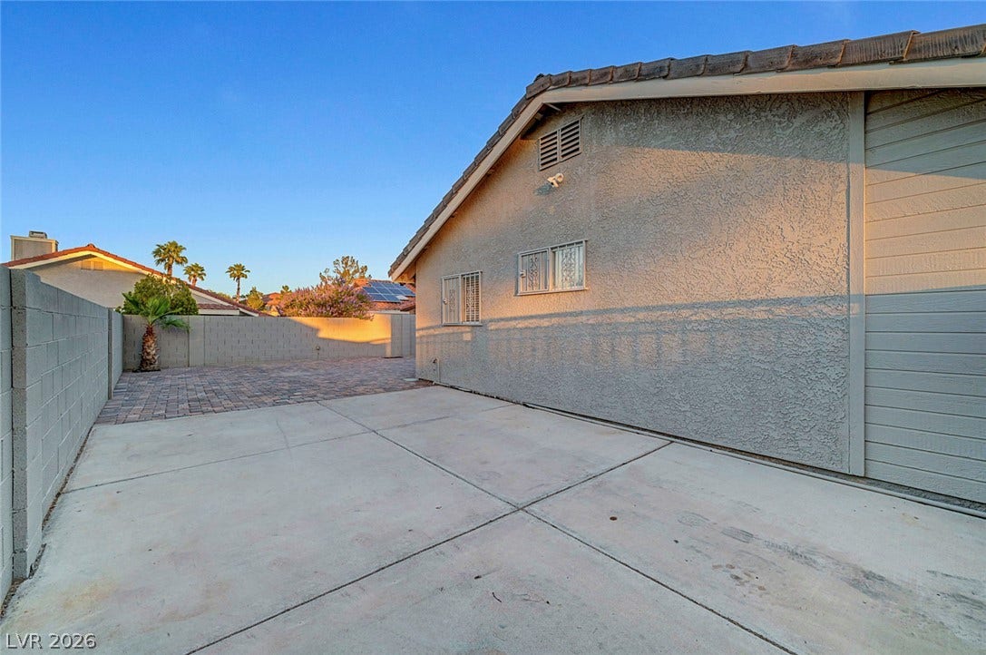 A spacious paved concrete side yard is enclosed by a privacy wall under clear blue skies.