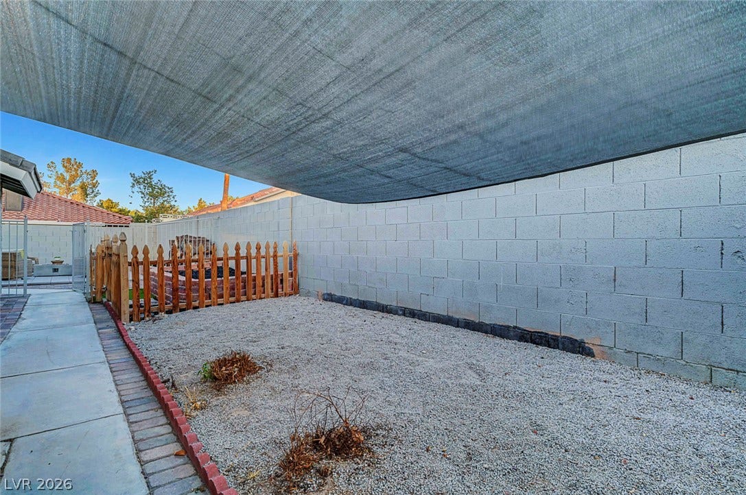 Shade sails cover a low-maintenance gravel yard enclosed by a block privacy wall.