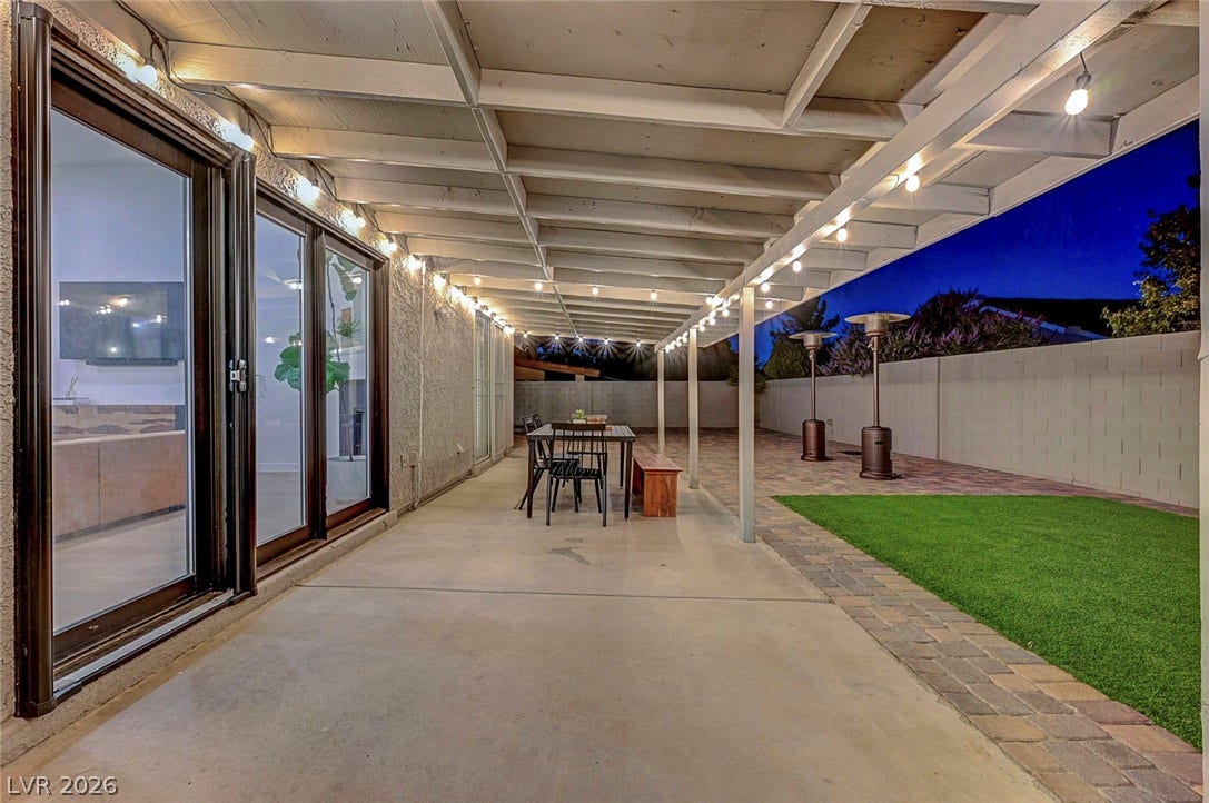 An extensive covered patio overlooks a private yard with brick paving and green turf.