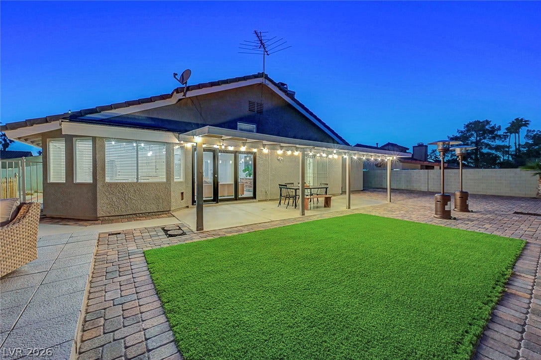 An inviting covered patio overlooks the manicured lawn and paved backyard setting.