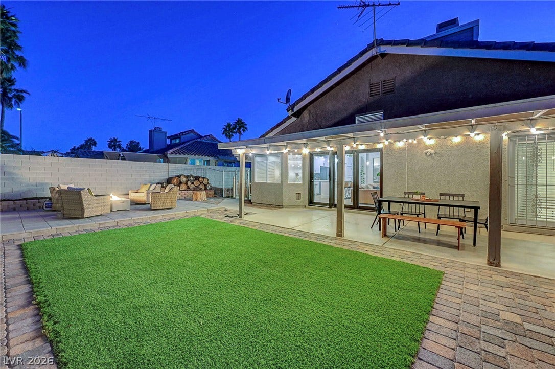 An inviting covered patio overlooks a manicured green lawn and a spacious paved courtyard.