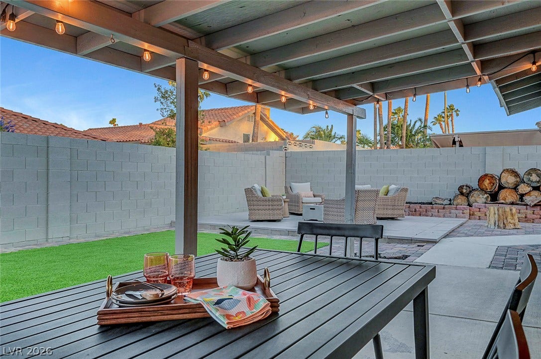 An inviting covered patio looks out over a private, fenced backyard featuring a paved terrace.
