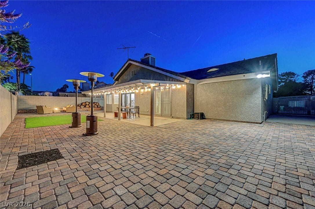 Extensive paver stone decking connects the covered patio with the open backyard lawn.