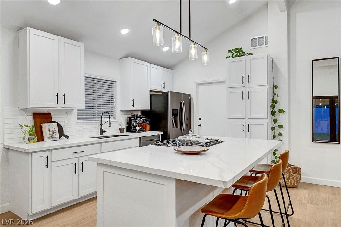 White cabinetry and stone counters define this modern workspace under high vaulted ceilings.