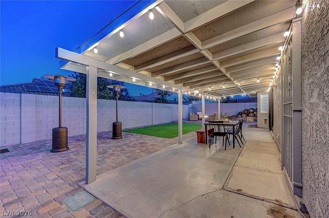 A sheltered concrete patio opens to a paved backyard under a clear evening sky.