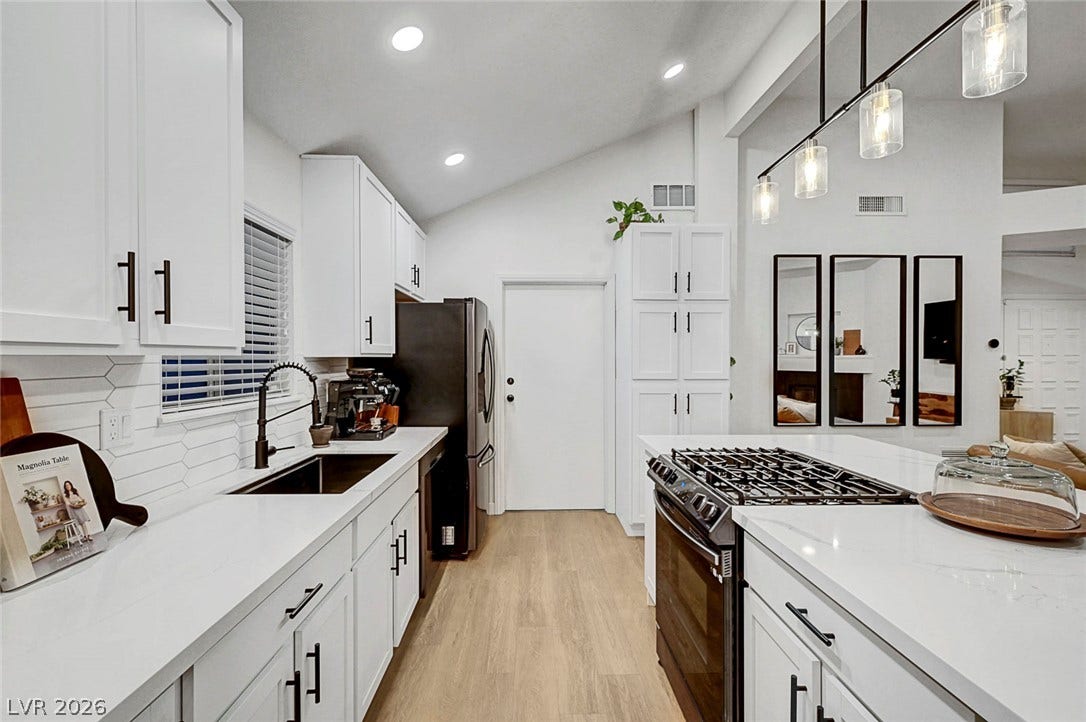 Vaulted ceilings and wood-style flooring elevate this modern kitchen featuring white cabinetry and stone countertops.