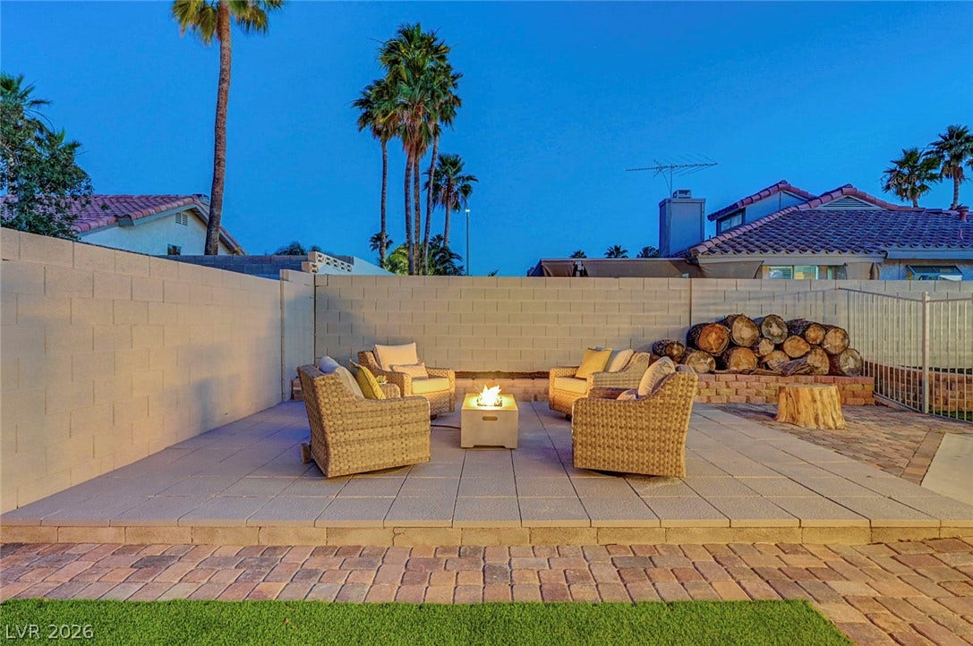 A spacious paved patio area features a warm central fire pit and privacy wall.