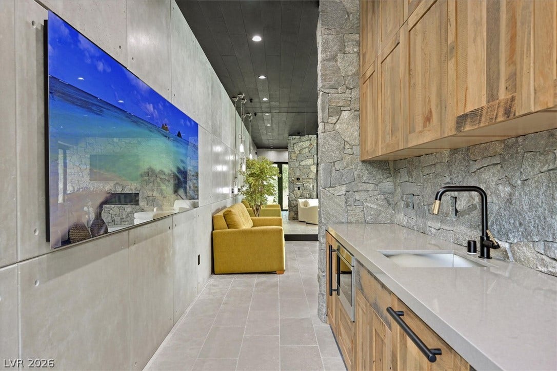 4155 Badura Avenue, Las Vegas, NV 89118 Concrete and stone walls create a striking modern hallway alongside custom wood cabinetry in the mini kitchen. The kitchenette includes a mini fridge, dish washer, and microwave.