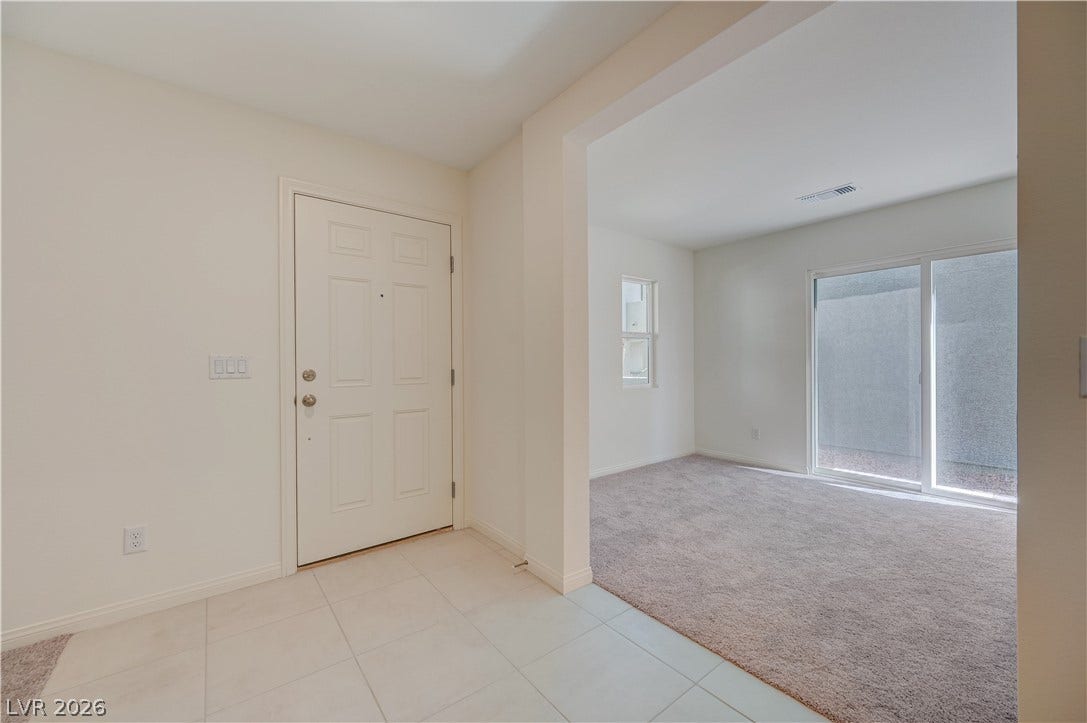 Tiled entryway leads directly into a carpeted living space with sliding glass doors.