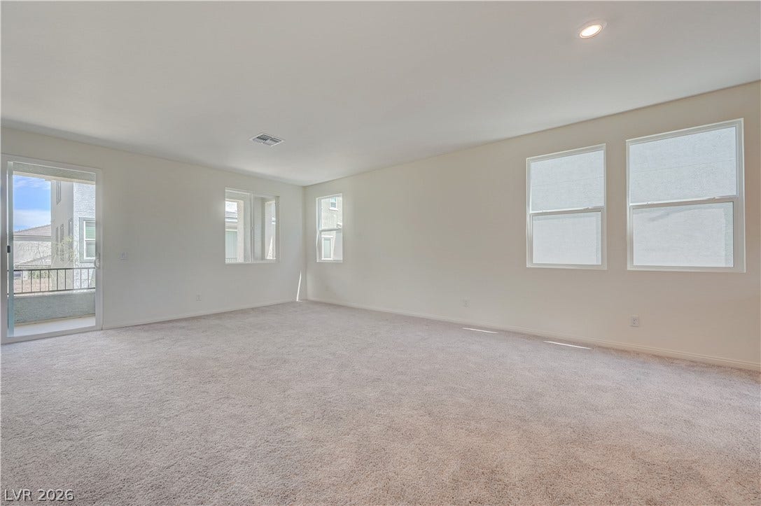 An open and airy living area boasts soft wall-to-wall carpeting and multiple large windows.