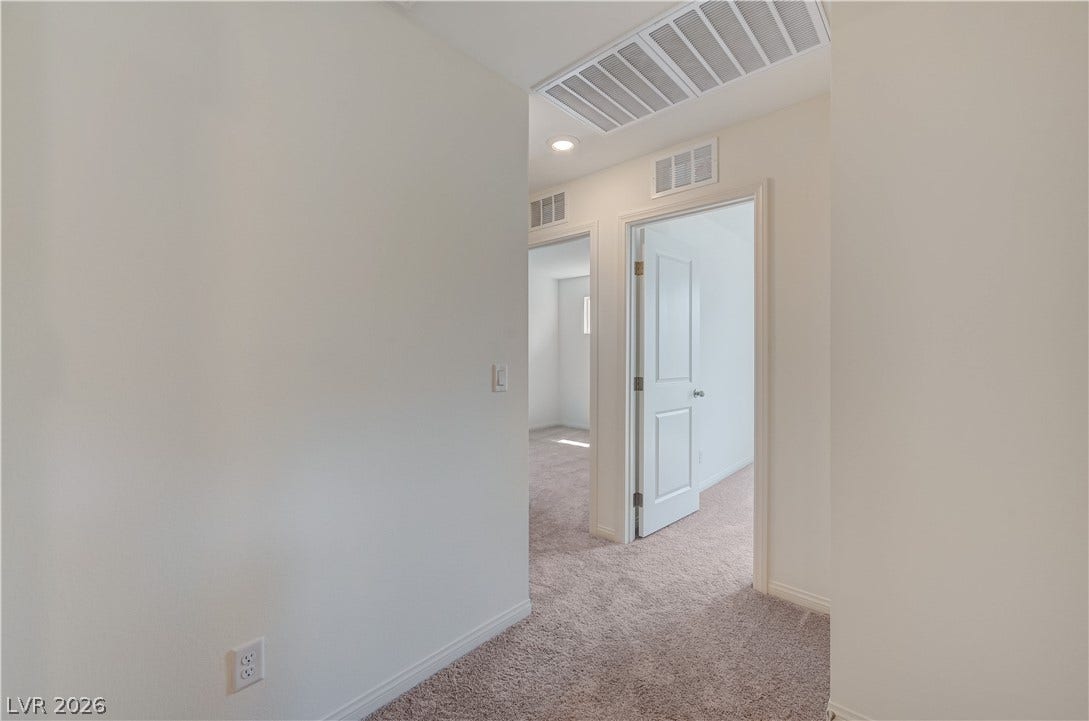 A clean transition space connects separate carpeted rooms through minimalist white doorways.