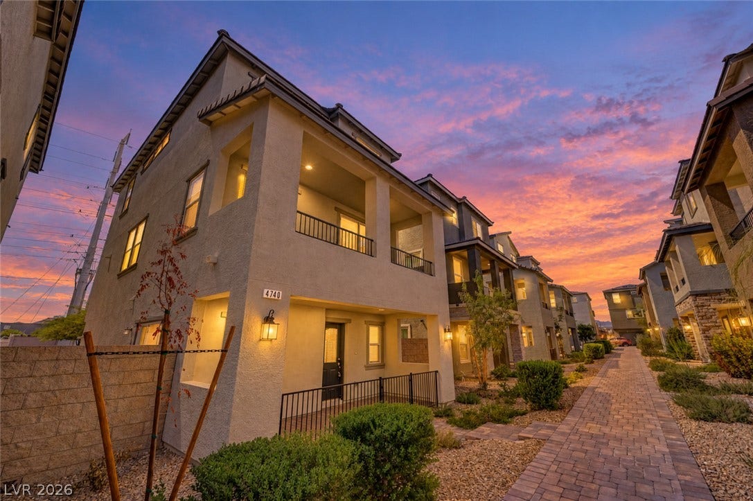 Multi-level modern townhomes stand elegantly along a neatly paved community walkway under a vibrant sunset sky.